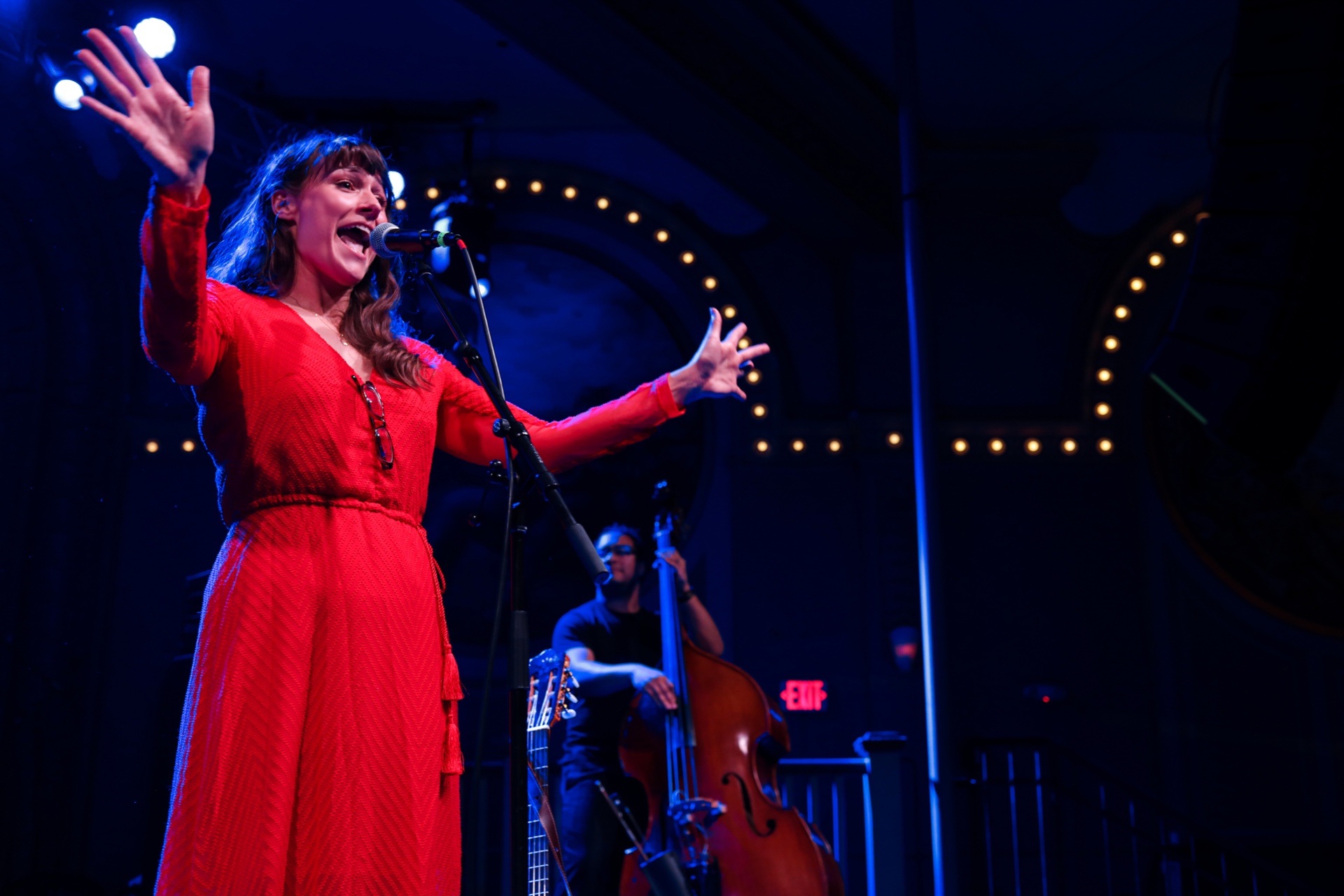 Stephanie Strange in a red dress plays on a moody stage with band